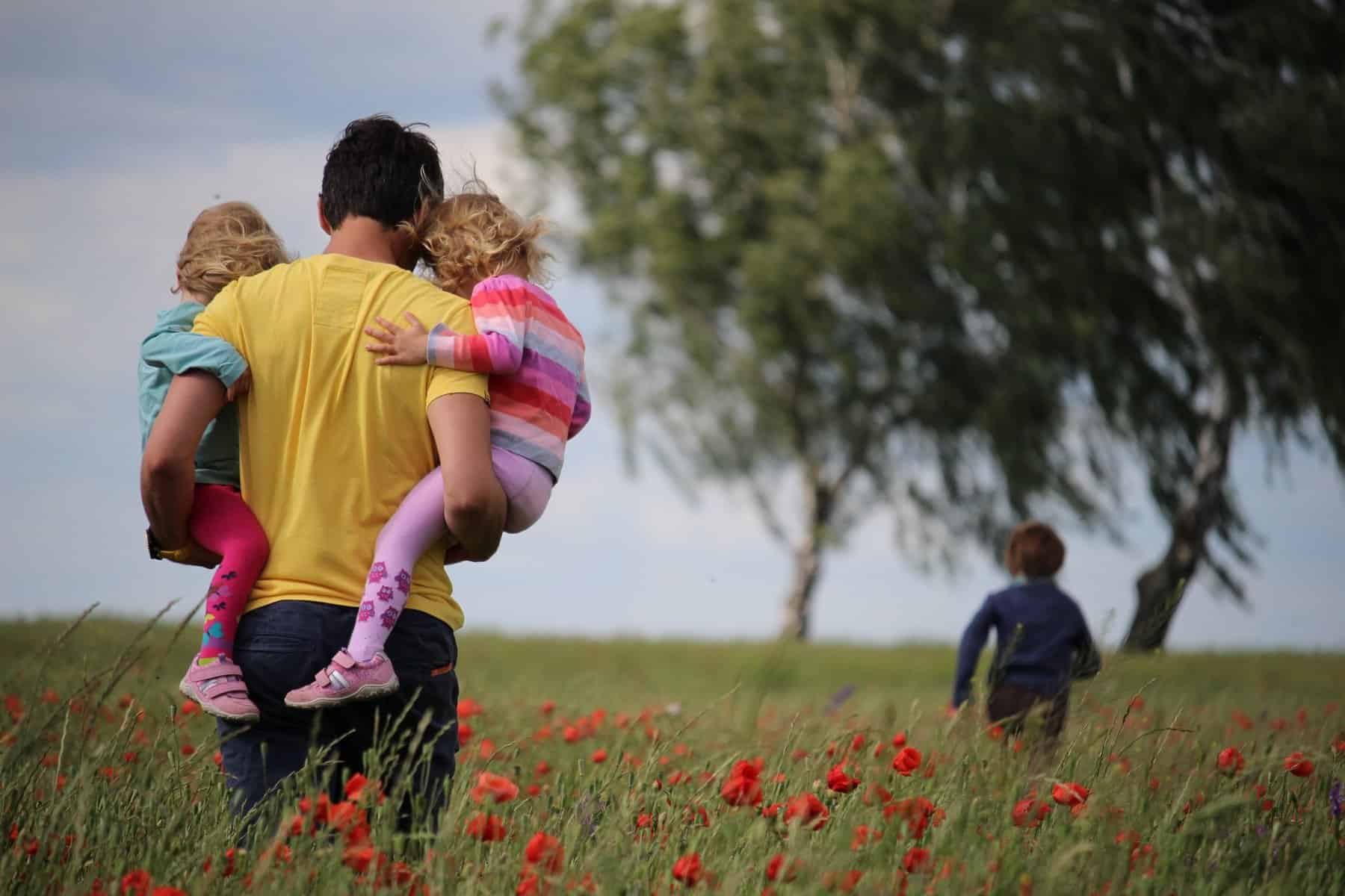 Father holding two of his daughters while on a field of grass. Porn addiction symptoms on dads