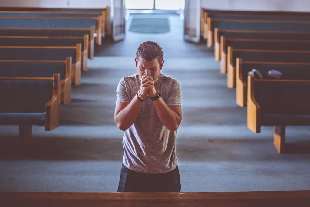 Man knelt in prayer in church. God wants us to break from porn addiction and enjoy all the benefits of quitting porn such as soul satisfaction, improved relationships and mood